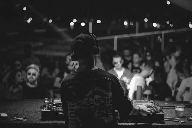Ein DJ legt nachts auf einer belebten Veranstaltung auf, während die Menge vor ihm tanzt und feiert, stimmungsvolles Clublicht im Hintergrund.