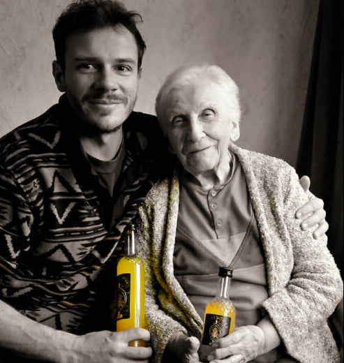 Ein junger Mann (Rafal) und eine ältere Frau (Krysia) sitzen eng beieinander und halten Flaschen mit gelbem Likör in den Händen – ein emotionales Porträt, das die familiären Wurzeln und die traditionelle Inspiration hinter der Marke zeigt.